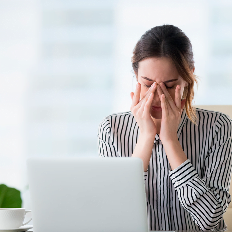 Mulher sentada em frente ao computador com as mãos nos olhos